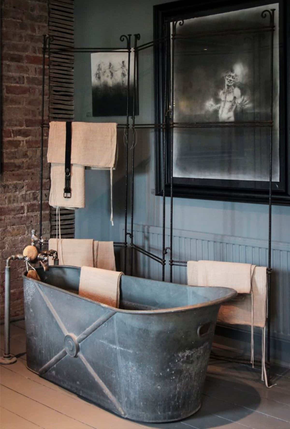 Metal bathtub with old industrial pipes and taps above it. Metal rod hangers next to bathtub