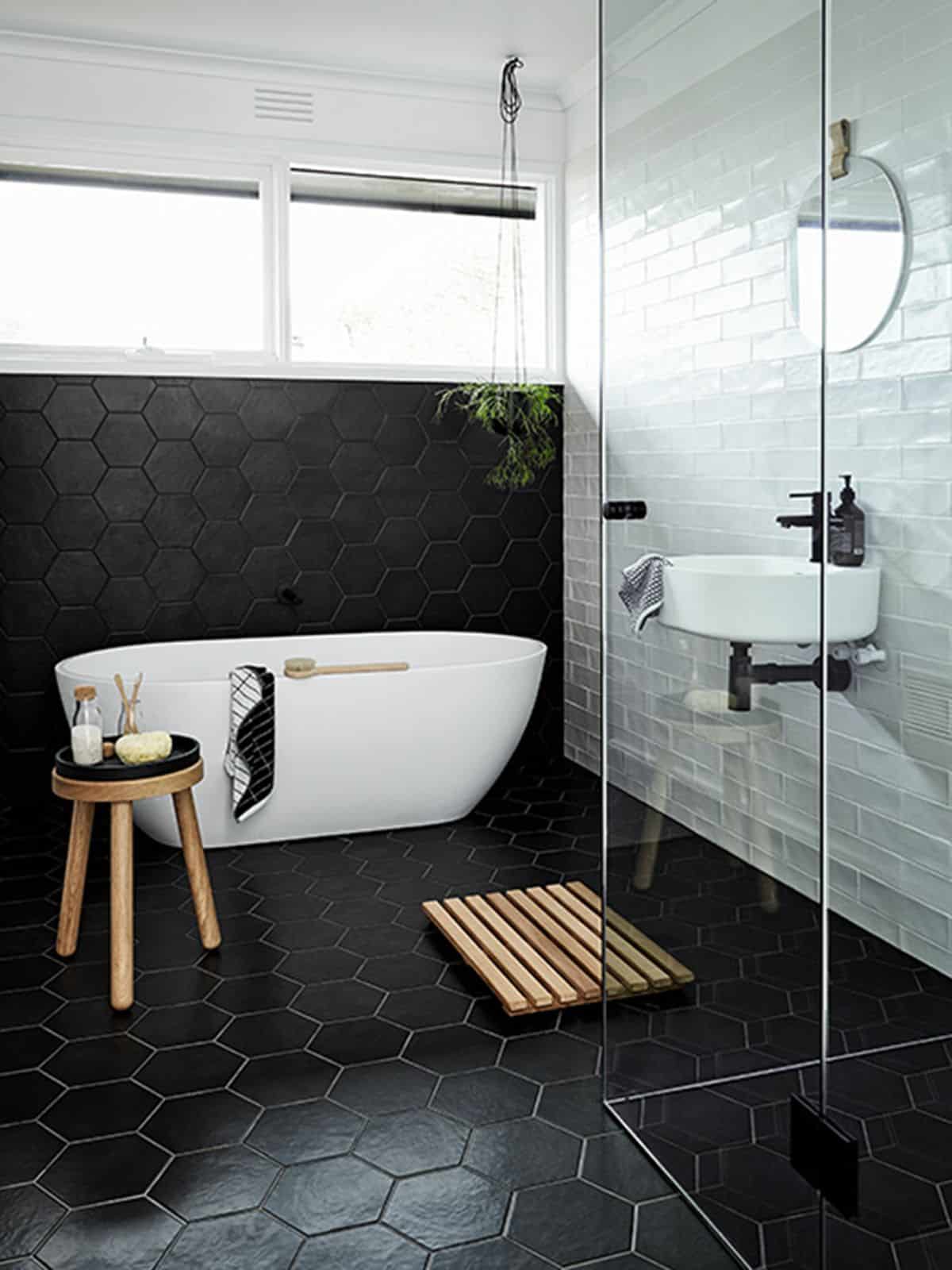 White bathtub along a black wall with hexagons and white masonry wall on other side
