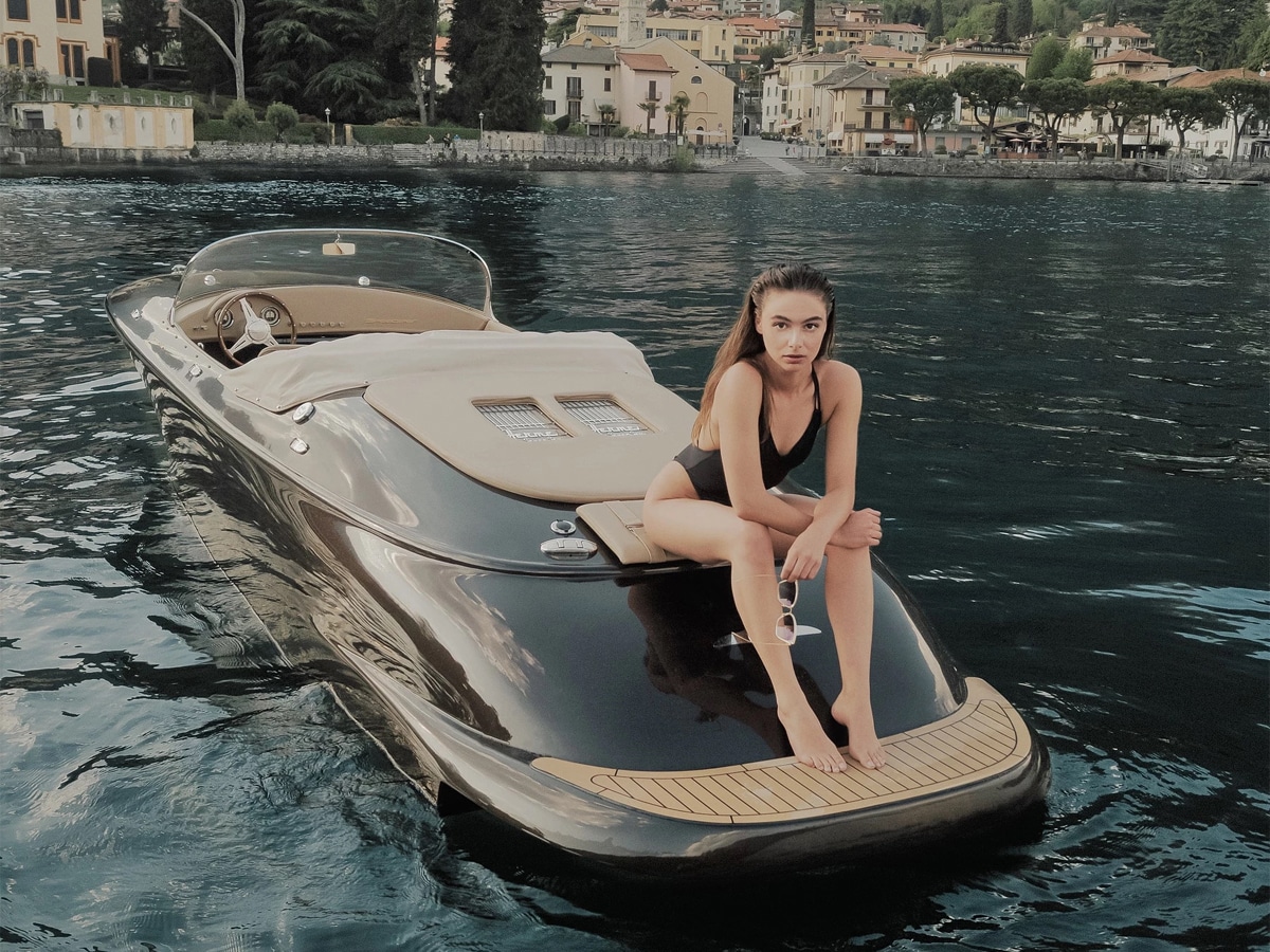 A woman in one-piece bikini sitting on rear of Hermes Speedster Boat