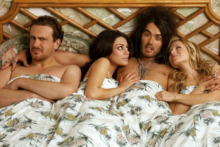 A man in bed with two women on his sides and a man on left with an angry face