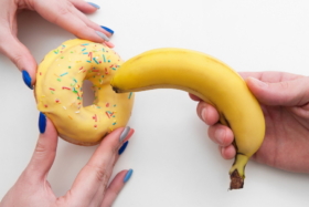 A hand pushing a banana towards a donut held by a pair of hands