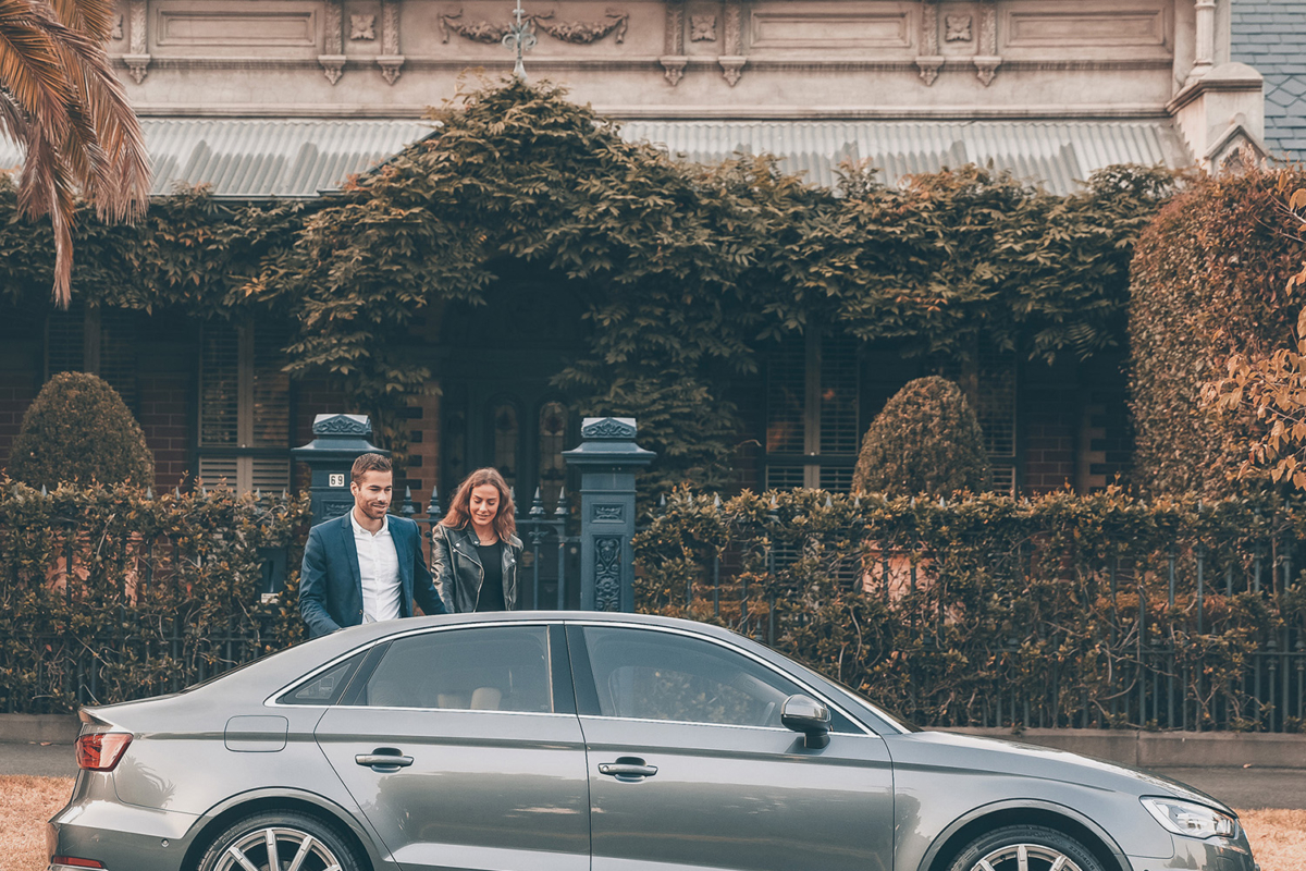 A man and a woman on the other side of a parked car