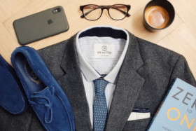 A Charcoal suit top part with phone, eyeglasses, cup of coffee, shoes around it