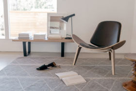 A chair with curved seat and a small table with books near wall in a room