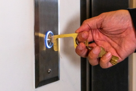 A hand using Hygiene Hand tool to push lift calling button