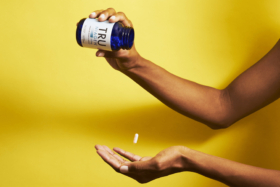 A hand dropping a pill out of TRU Niagen bottle