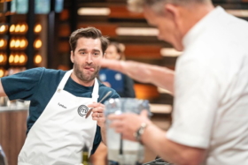 A contestant with his tongue out looking at Gordon Ramsay working a mixer on MasterChef Australia