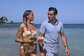 A man and a woman in bikini walking on a beach
