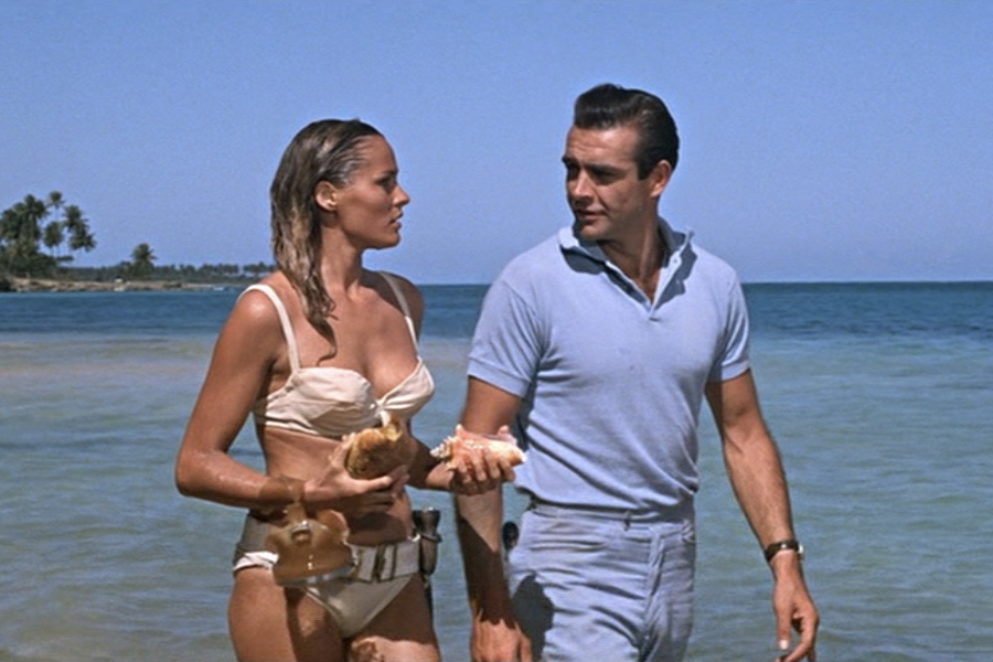 A man and a woman in bikini walking on a beach