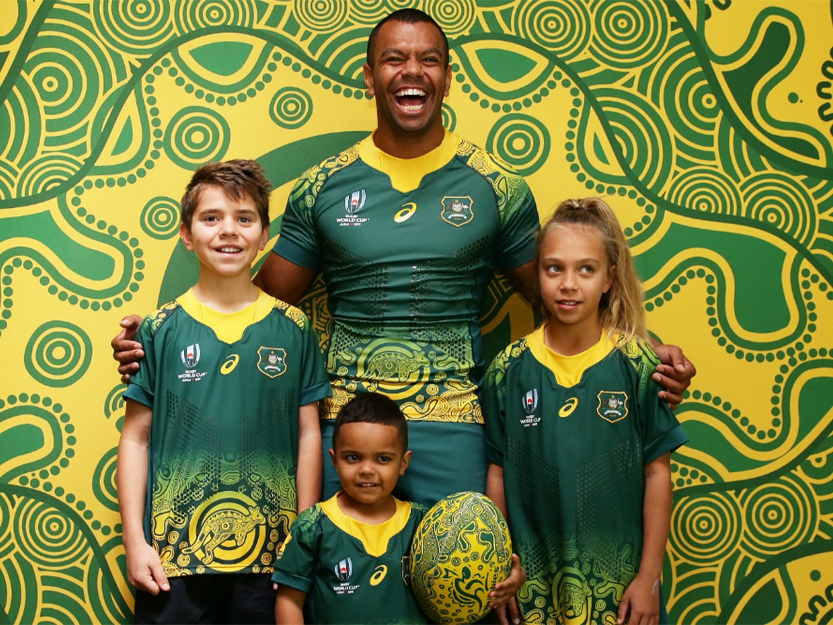 An Australian Rugby team player posing with three kids in Australian Rugby jerseys
