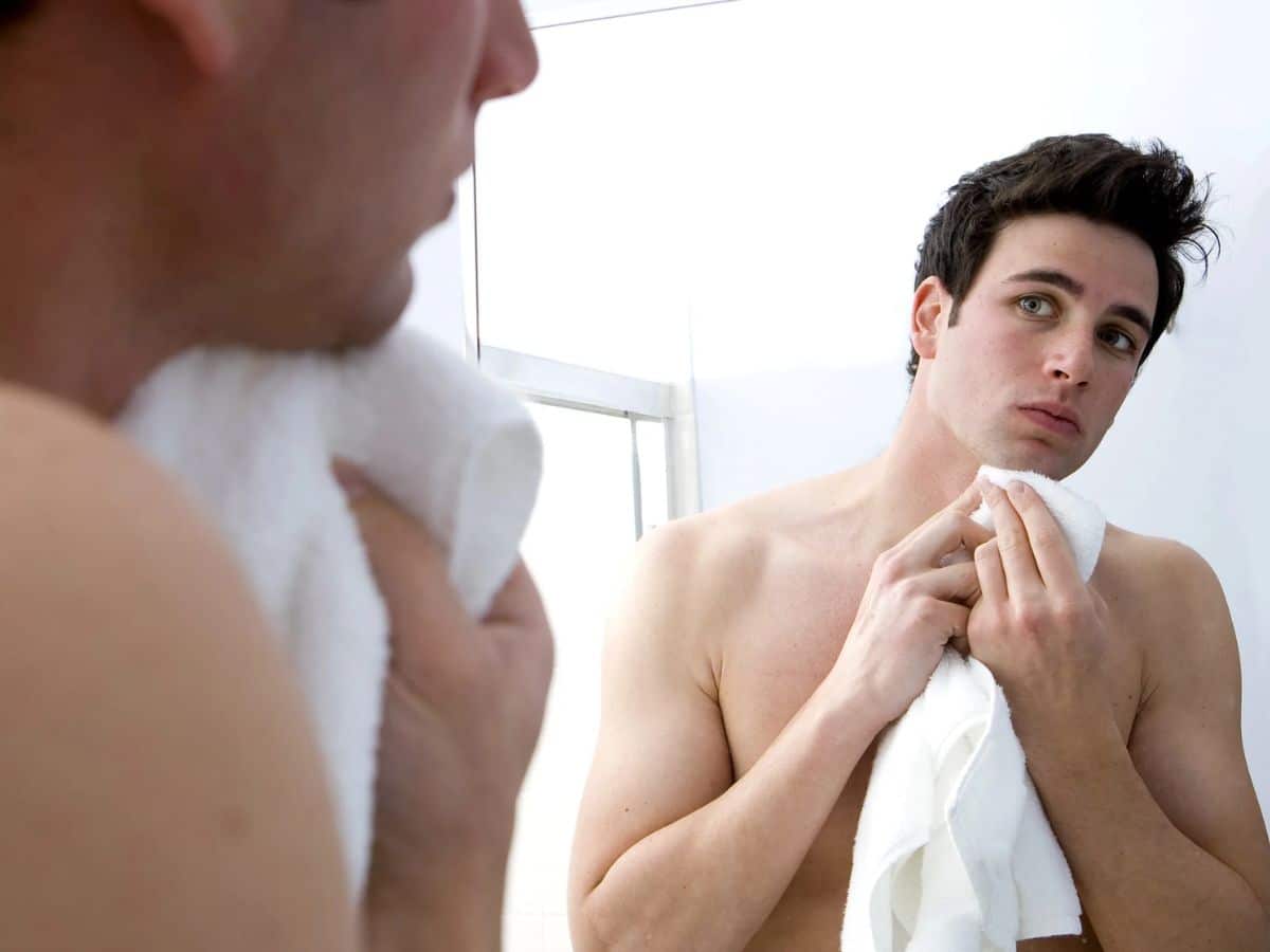 A man looking in mirror cleaning himself with a towel