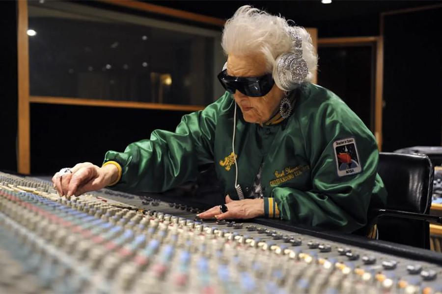 An old woman on a music system wearing silver headphones and black glasses