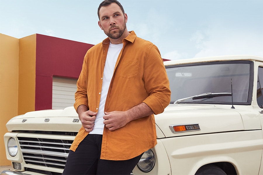 A model leaning on front hood of  a Ford truck wearing an orange shirt over a white t-shirt from Johnny Bigg