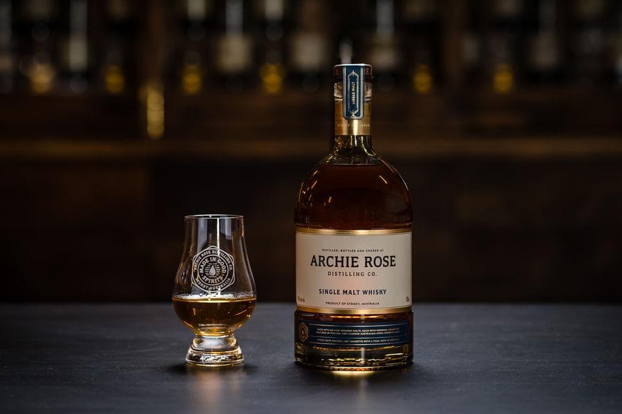 A glass and bottle of of Archie Rose Single Malt whiskey