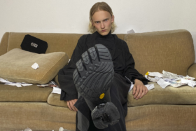 Sole of Balenciaga Toe Sneaker raised to camera in focus with the model wearing it sitting on a sofa in background
