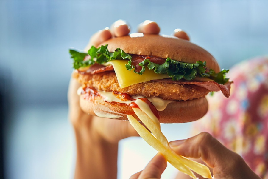 A pair of hands holding fries and McDonald's Chicken Parmi Burger
