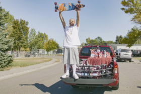 DoggFace holding his skateboard in air with both hands standing in cargo of his truck