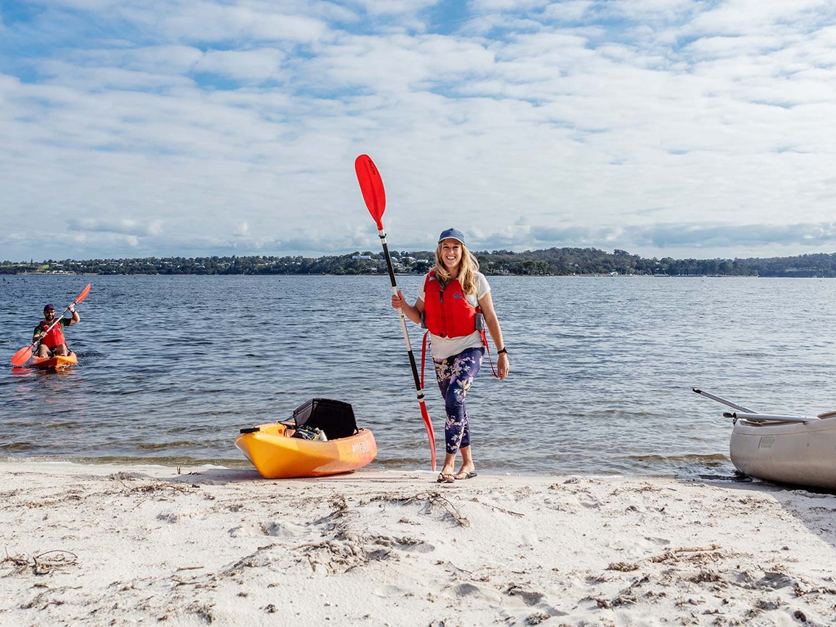 smiling woman with a kayak standing on the beach at spoon bay Gippsland lakes coastal park
