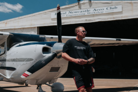A man in a 257 Collective t-shirt standing leaning on a small plane's front propeller