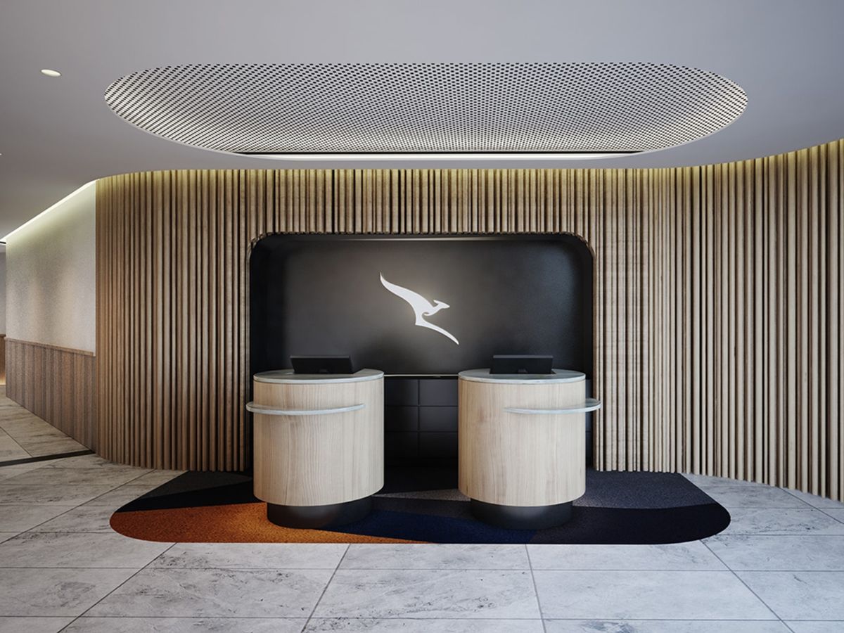 Two counters with screens at airport lounge with Qantas logo on wall behind the,