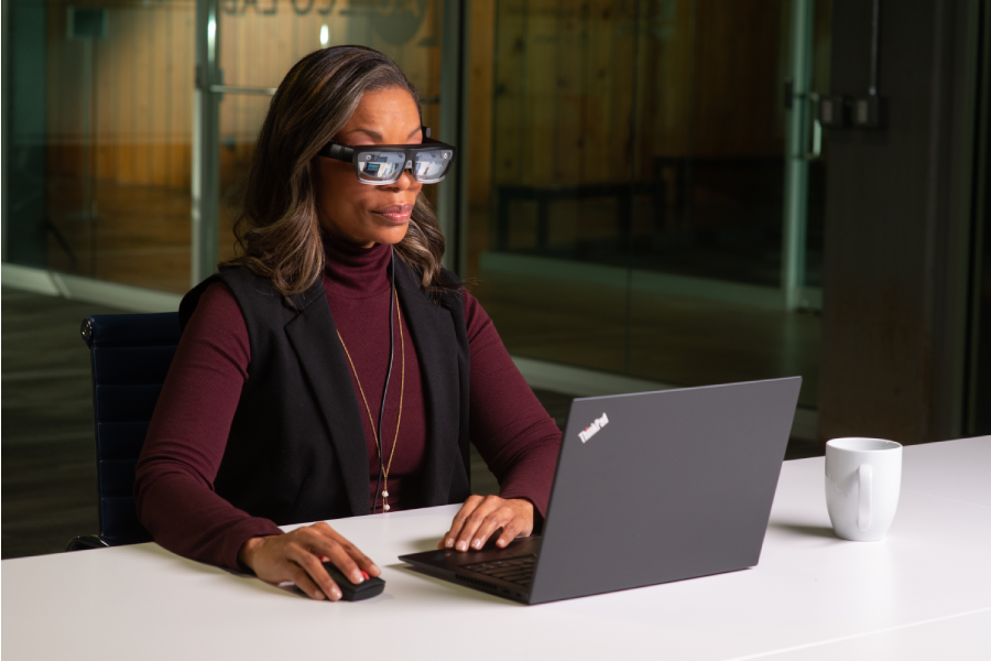 A woman wearing Lenovo’s ThinkReality A3 Smart Glasses working on a laptop