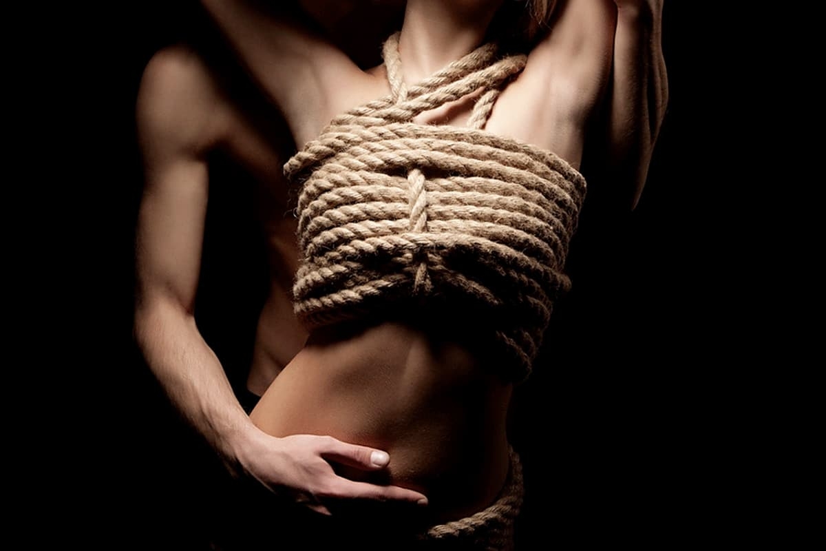 A woman with rope tied around her chest. Man holding the woman's stomach from behind.
