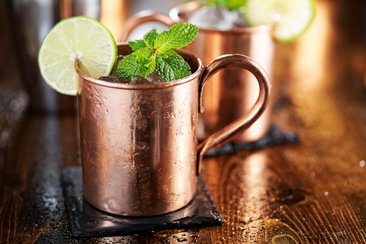 Copper mug with Moscow Mule cocktail garnished with mint and lime slice on a wooden table.