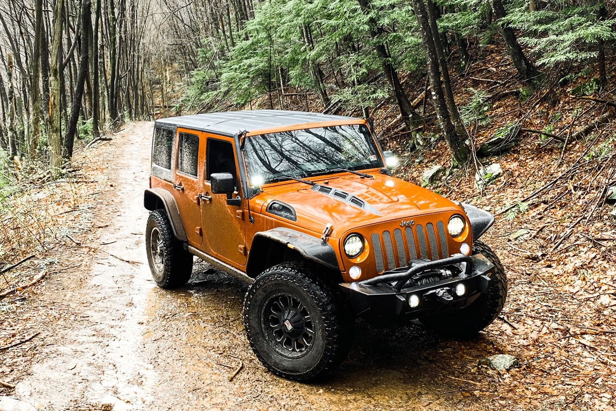 A rust orange Jeep on a forest trail