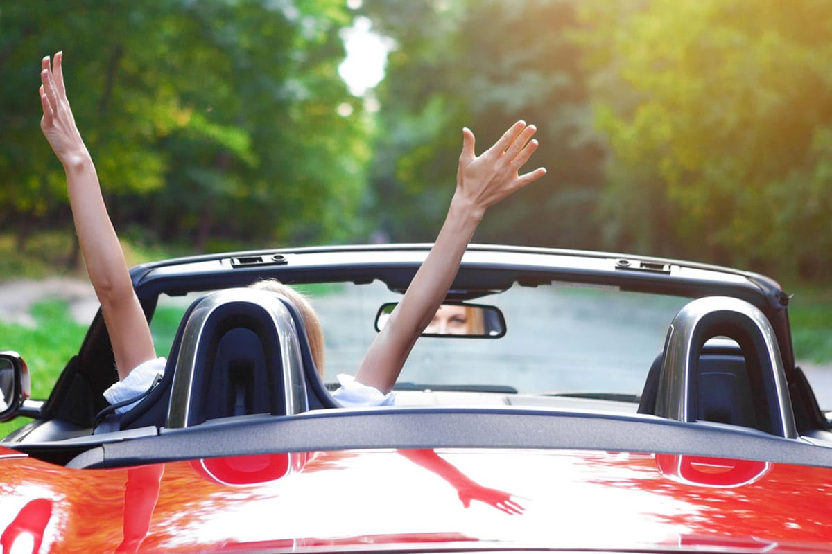 A person with hands thrown in air on the front seat of a convertible car
