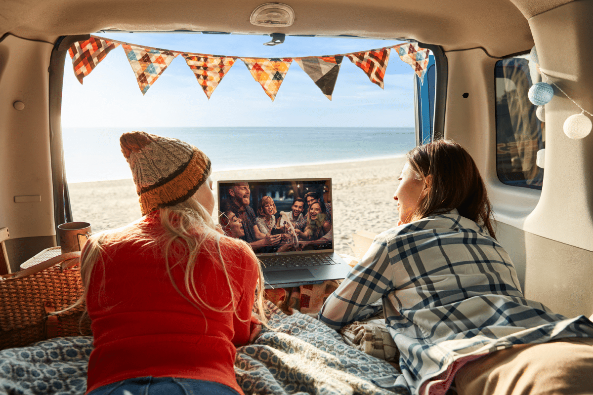 Two women friends inside a camper van watching a movie with a laptop