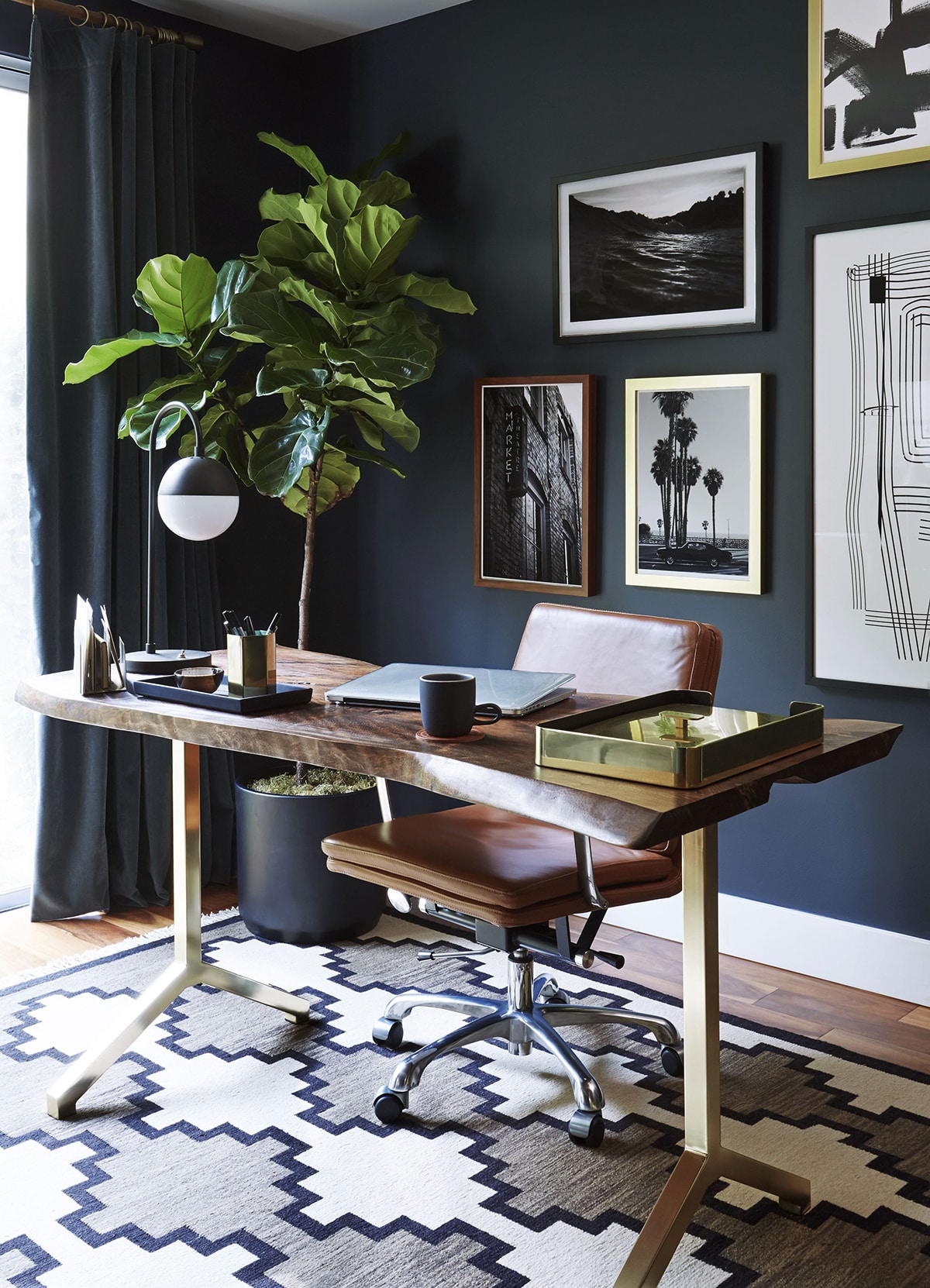 Office table in front of a blue wall with framed photos and a plant in a corner