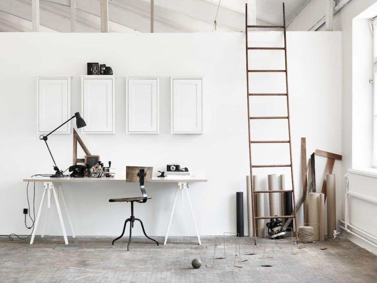 White home office with four cabinets above table on wall and a ladder leaning on wall next to it