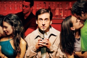 Steve Carell drinking with a straw at a bar  as two couples make out on his sides in a poster from The 40-year-old virgin 