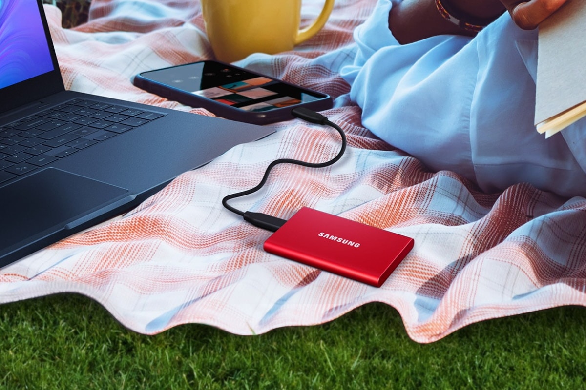 Samsung Portable 2TB SSD T7 connected to a laptop beside a man on a picnic blanket