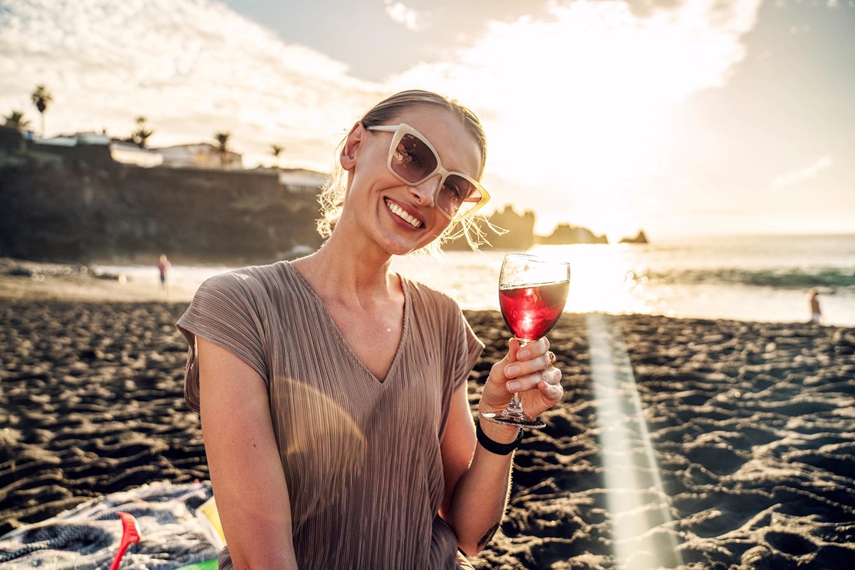 young woman is sitting on sea beach with wineglass of wine 