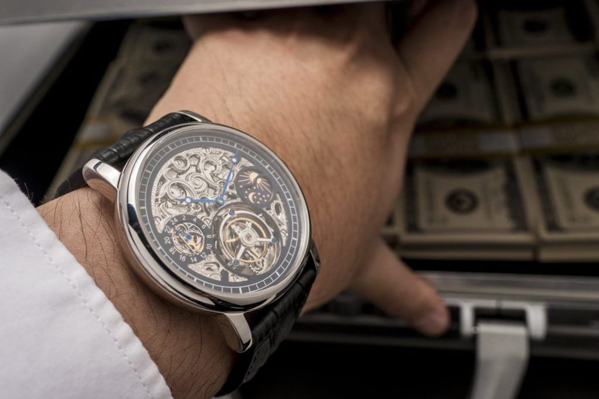 tourbillon watch on man's hand in front of money