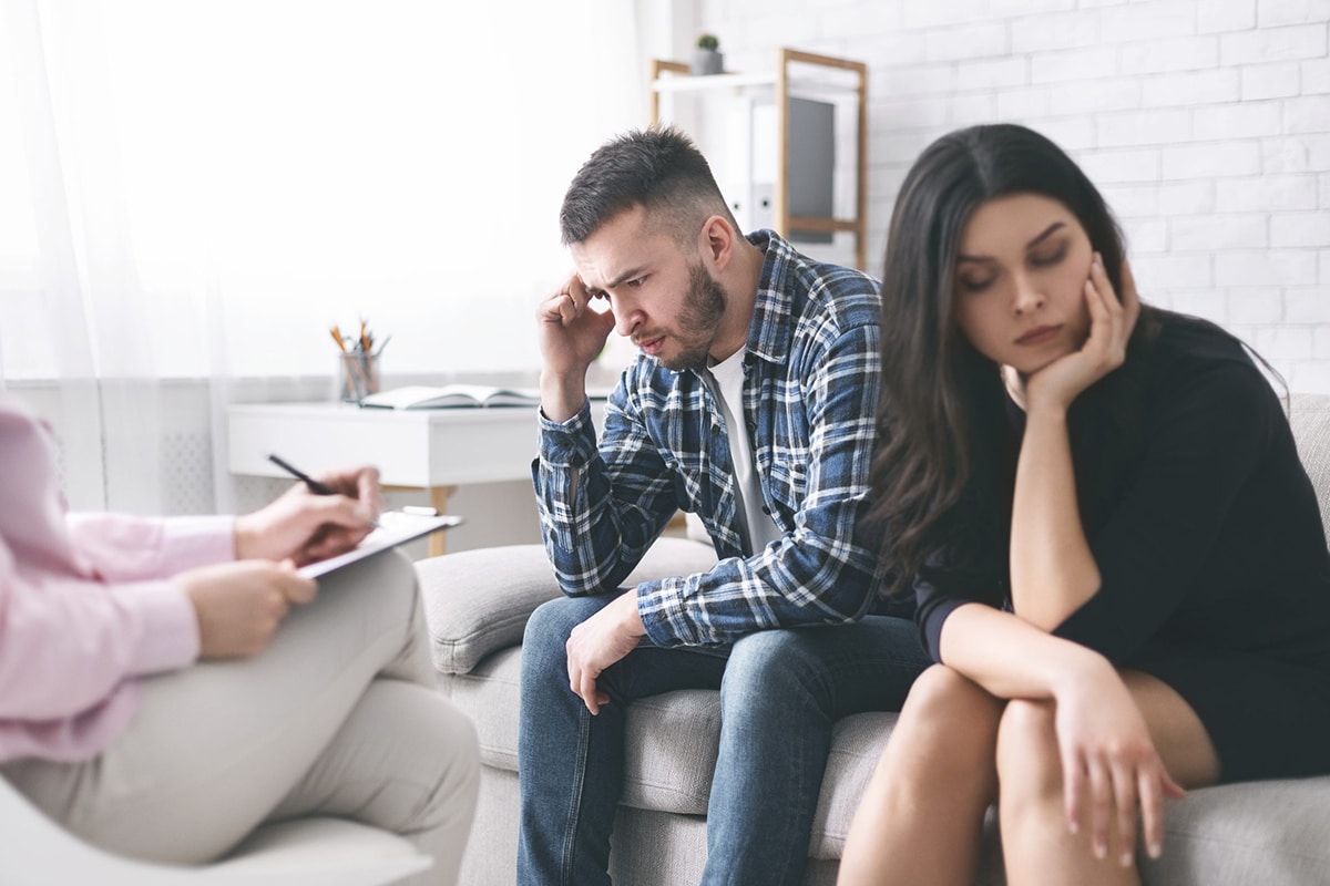 stressed couple sitting on coach at psychologist cabinet