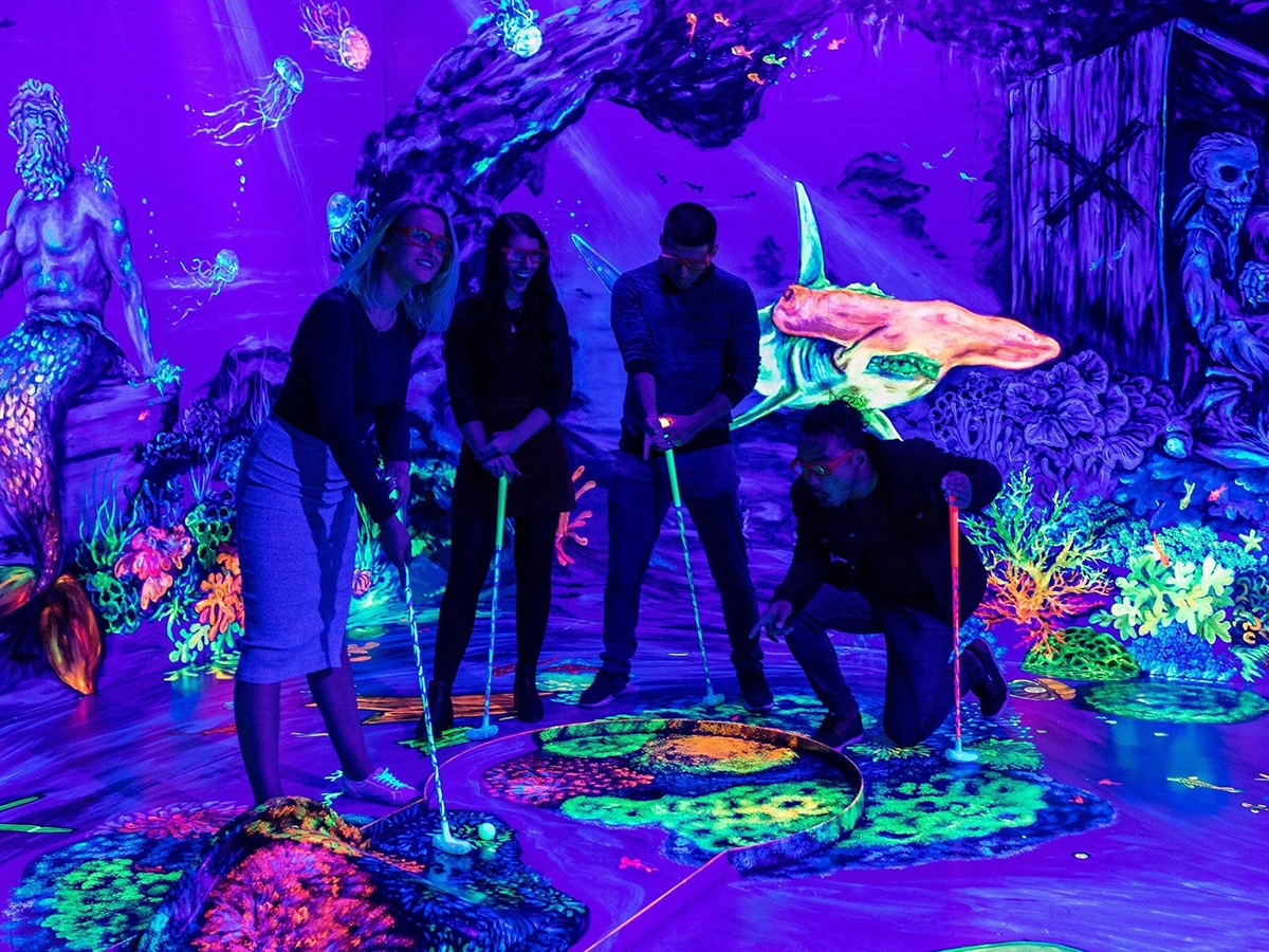 group of people playing minigolf at glowing rooms