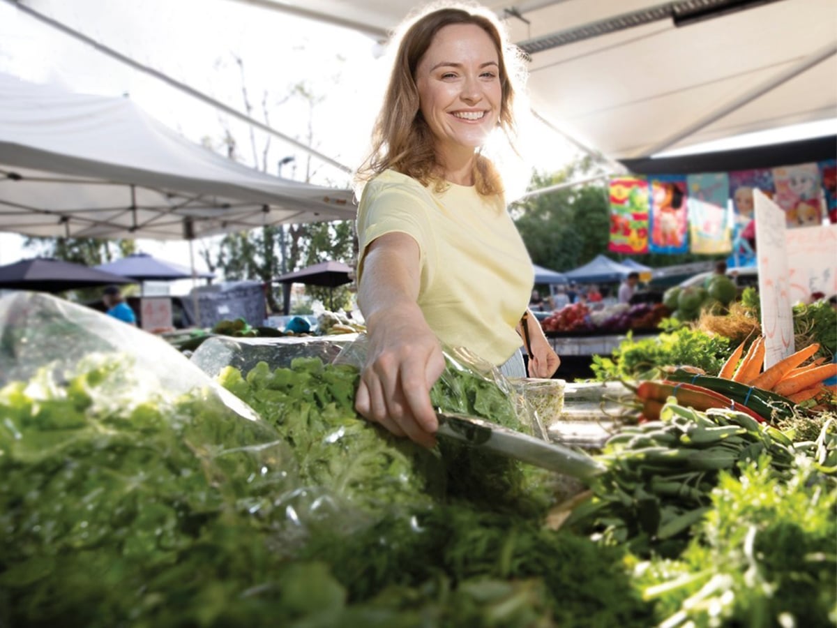 smiling woman selecting greens on showcase at saturday fresh markets