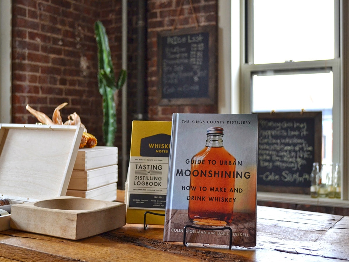 guide to urban moonshining how to make and drink whiskey book standing on wooden table