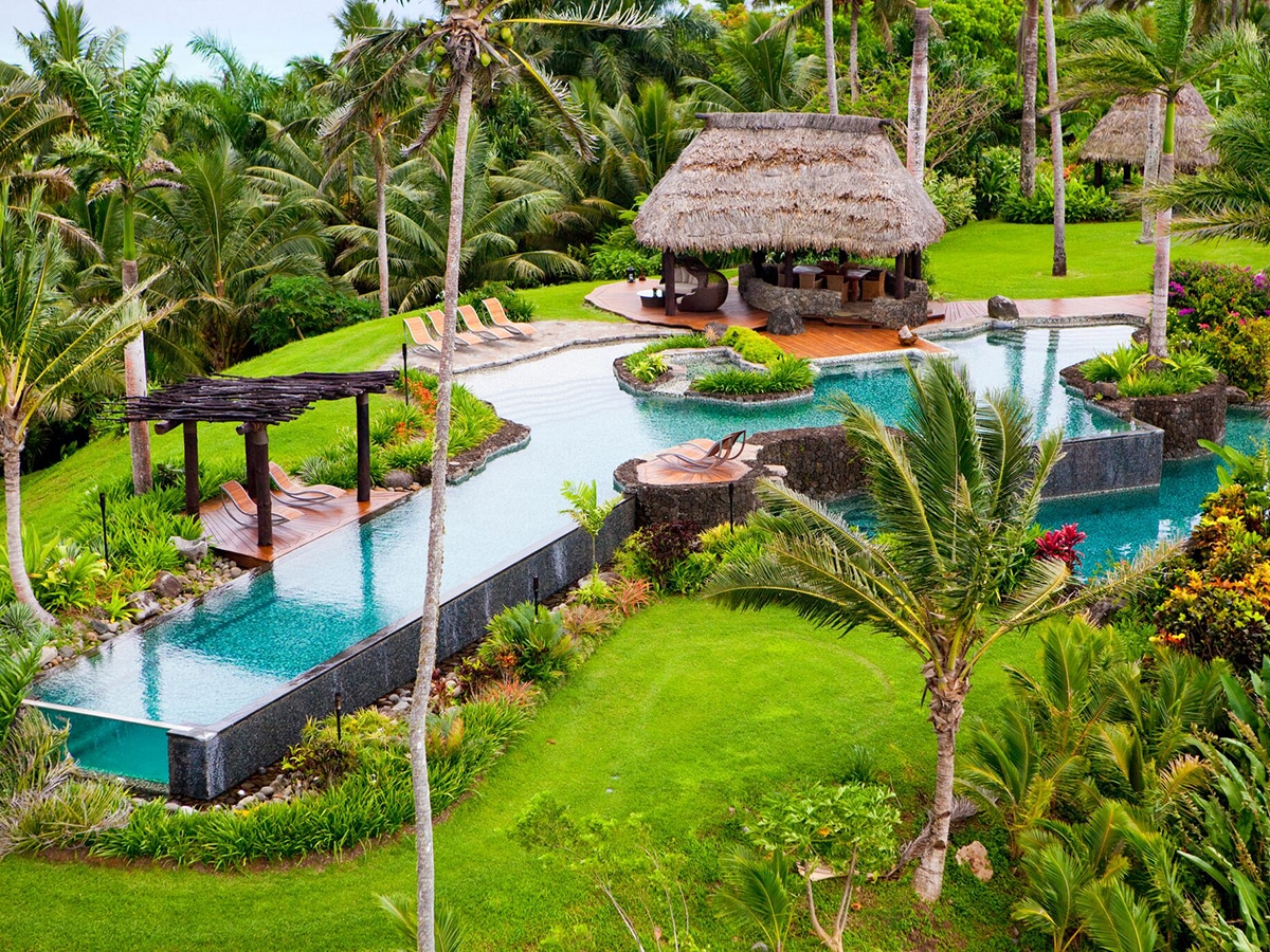 High angle shot of The Hilltop Villa outdoors with a long pool and huts surrounded by coconut palm trees