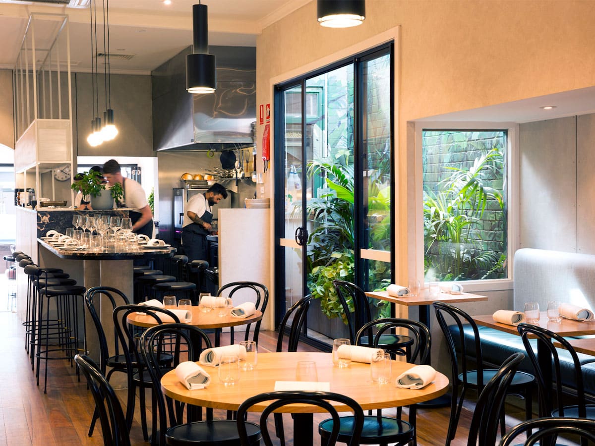 Interior of Etta restaurant with white, cream and black colour scheme showing tables and chairs with staff behind the bar counter