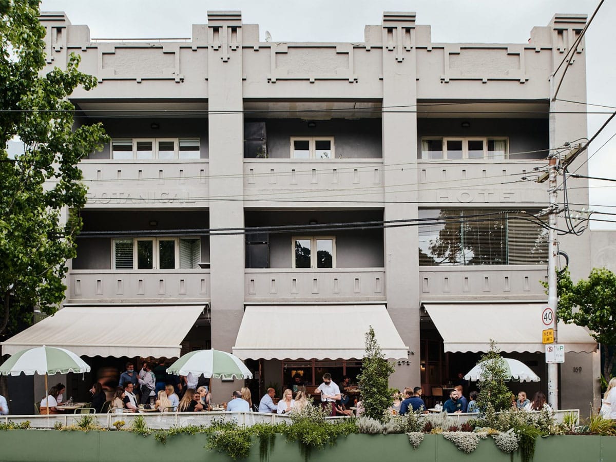 Exterior of Gilson restaurant with grey and white colour scheme showing white and green patio umbrellas and customers dining outside