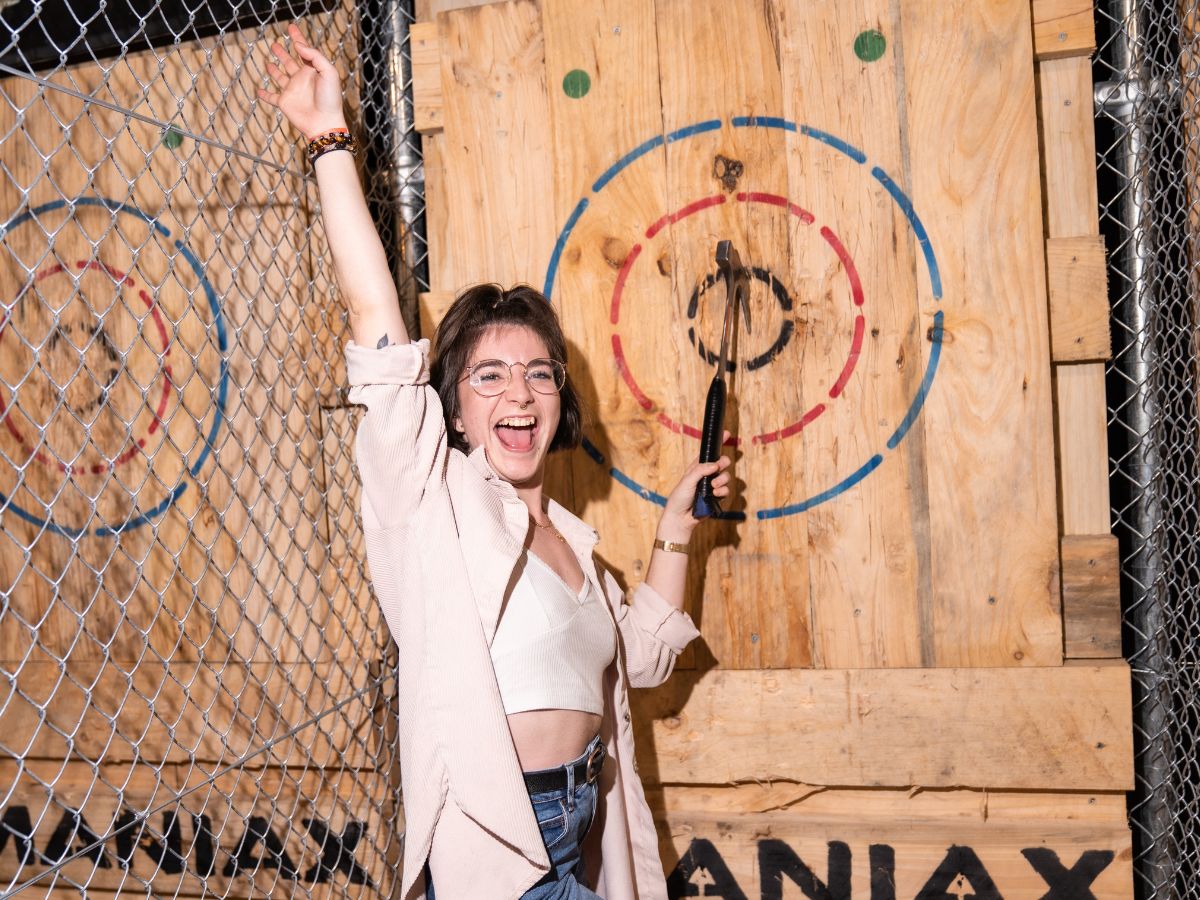 Woman posing for the camera while holding the axe impaled in the wood target