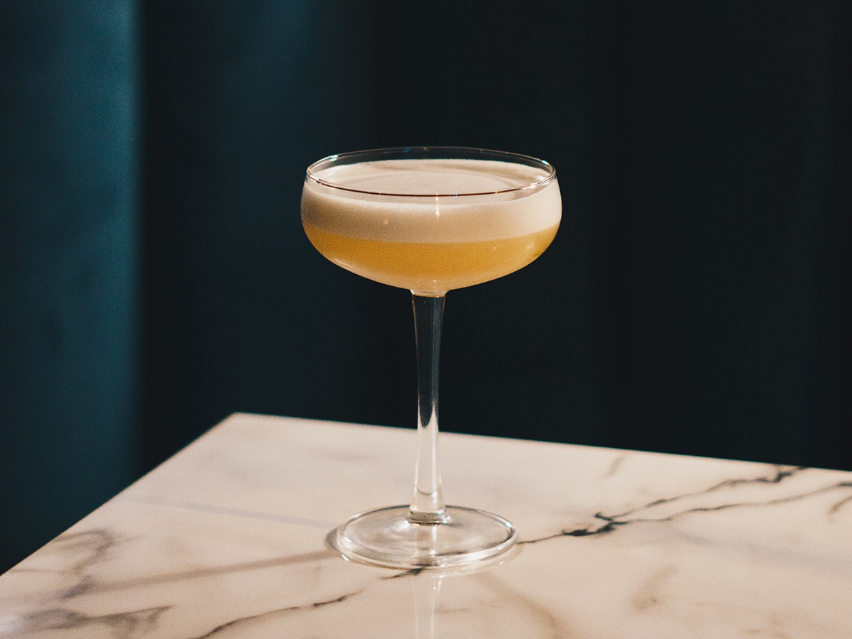 A glass of whisky sour set on top of a marble bar