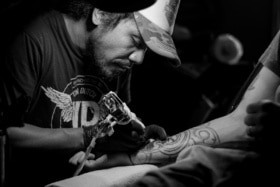Black and white image of a tattoo artist inking a man's forearm