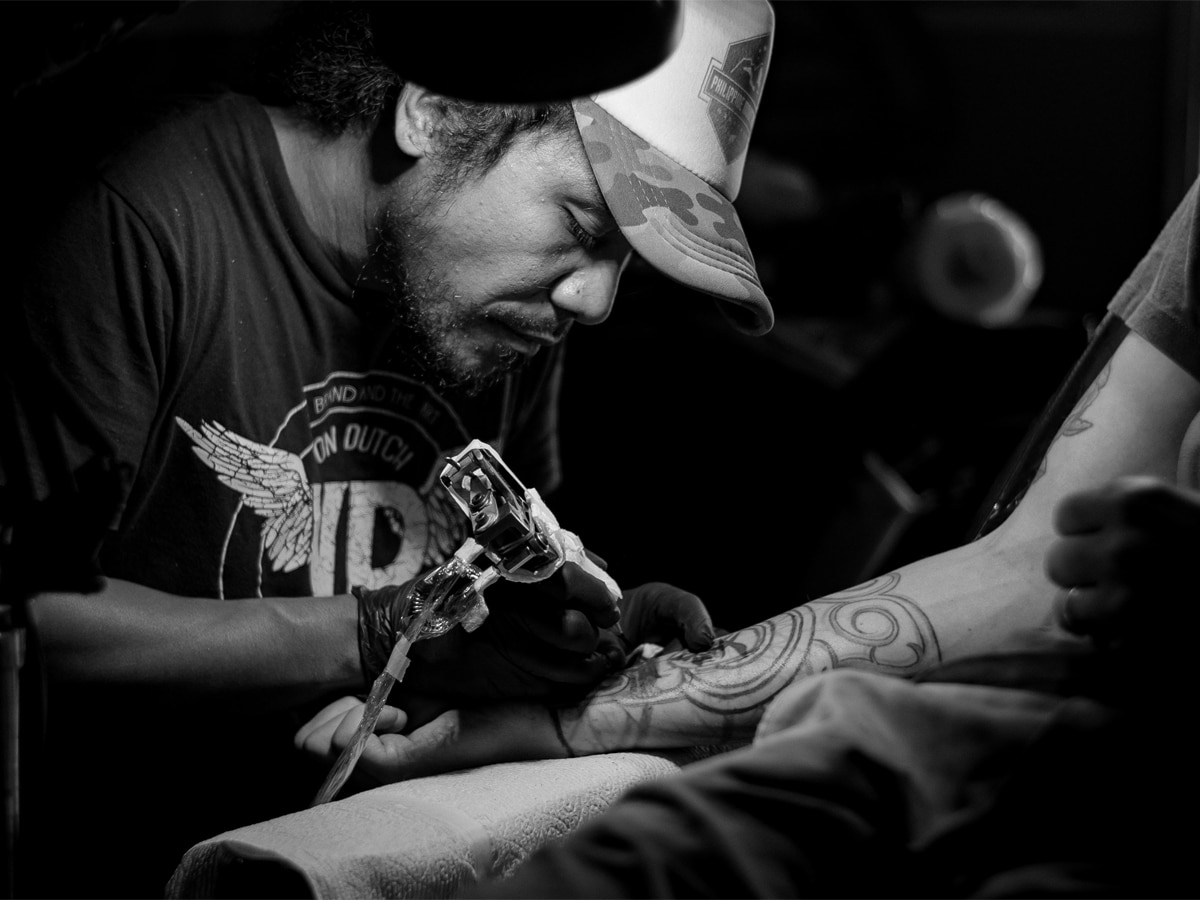 Black and white image of a tattoo artist inking a man's forearm