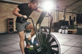 Man in sportswear sitting on cycling machine and riding fast in modern gym