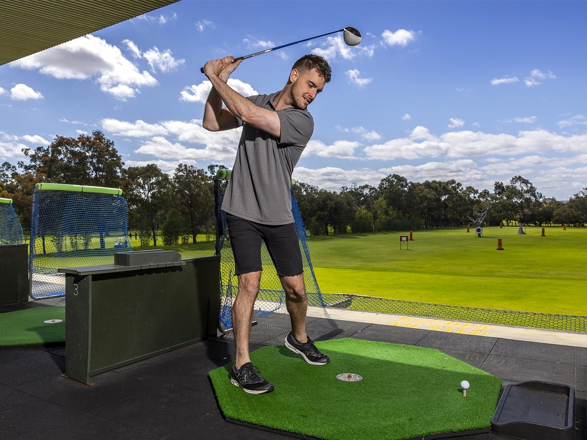 Full shot of a man aiming to hit a golf ball at the Whaleback Golf Course driving range