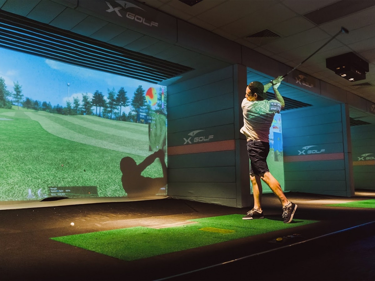 Full shot of a man hitting a golf ball in an indoor driving range at X-Golf Balcatta